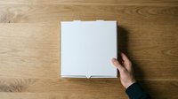 Open white box on wooden surface with hand reaching toward it, overhead view for product packaging and delivery concepts.