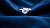 Elegant diamond solitaire engagement ring on luxurious blue silk fabric with dramatic lighting for wedding and jewelry advertising campaigns.