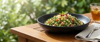 Colorful quinoa salad with vegetables served in black bowl on wooden table outdoors, fresh healthy lunch option for meal planning and nutrition content.
