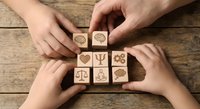 Hands arranging wooden blocks with psychology and mental health symbols on rustic wood surface for therapy and wellness concepts.
