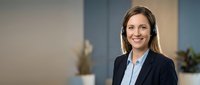 Professional young Caucasian businesswoman with headset smiling confidently in modern office environment for customer service and corporate communications.