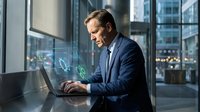 Professional businessman working on laptop with holographic data visualization in modern office environment for corporate technology presentations.