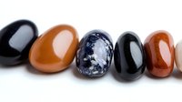 Polished semiprecious stones lined up in row showing natural patterns and colors of black obsidian, carnelian, sodalite and agate on white background.
