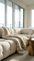 Cozy modern living room with cream curved sofa, knit throw blanket, wooden side table, and floor-to-ceiling windows overlooking balcony for interior design and home decor projects.