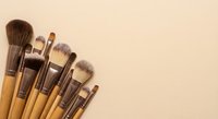 Professional makeup brushes with wooden handles arranged on neutral beige background for cosmetic application and beauty routine essentials.