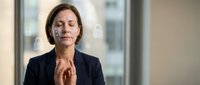Professional businesswoman with closed eyes practicing mindfulness meditation in modern office environment for stress relief and mental wellness.
