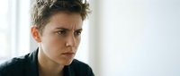 Young woman with short curly hair showing concerned worried expression in natural light. Professional headshot for mental health awareness campaigns.