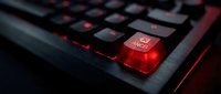Gaming keyboard with glowing red enter key and backlit keys for esports and computer gaming setup in dark environment.