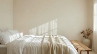Serene bedroom with unmade white bedding, natural sunlight streaming through window, minimalist decor with dried flowers in vase on wooden nightstand.