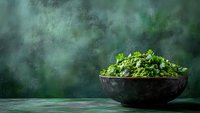 Fresh green salad with mixed herbs and leafy vegetables in rustic ceramic bowl against dark moody background, food photography styling.