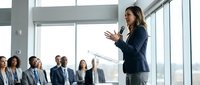Professional businesswoman presenting to corporate team in modern conference room with city view through large windows during executive meeting.