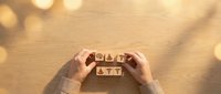 Hands arranging wooden letter blocks spelling BUY and SELL on warm textured surface with soft bokeh lighting for trading and investment concepts.