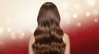 Young woman with long wavy brown hair from behind against red bokeh background with sparkles for beauty salon advertising and hair care products.