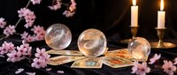 Mystical fortune telling setup with crystal balls, tarot cards and candles surrounded by pink cherry blossoms for spiritual guidance and divination practices.
