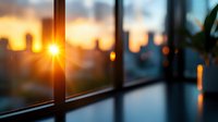 Dramatic sunset view through modern window frame with sun rays creating lens flare effect, silhouetted cityscape in background creates peaceful urban atmosphere.