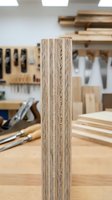 Plywood edge detail in carpentry workshop showing layered wood construction with tools and lumber materials in blurred background for woodworking projects.