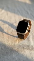 Modern smartwatch with brown leather strap on textured fabric surface with natural sunlight shadows creating elegant minimalist lifestyle composition.
