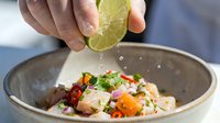 Hands squeezing fresh lime juice over Asian noodle bowl with vegetables and protein, culinary preparation and cooking concept for food service and restaurant use.