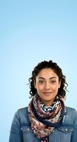 Young woman with curly dark hair and medium skin tone wearing denim shirt and patterned scarf against light blue background for portrait use.
