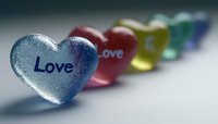 Colorful glass hearts with love text arranged in row creating rainbow effect against blurred background, romantic valentines concept for greeting cards.