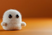 Cute white plush toy ghost with black button eyes on orange background, soft textile handmade character for Halloween decoration and children play.
