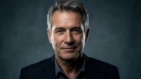 Professional mature Caucasian businessman with gray hair in black shirt against dark background for corporate headshot and executive portrait use.