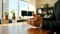 Professional businessman hands gesturing during office meeting or presentation in modern workplace with natural lighting and plants.