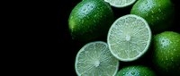 Fresh green limes with water droplets on dark background, whole and sliced citrus fruits for cooking, cocktails and healthy nutrition concepts.