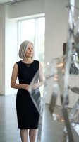 Confident mature Caucasian businesswoman in black dress standing by modern staircase in corporate office building for professional business concepts.