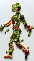 Fresh vegetables arranged in shape of running human figure with carrots, broccoli, tomatoes, and lettuce on white background. Creative healthy lifestyle concept.