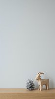 Wooden goat figurine and gray pinecone on wooden surface against neutral wall background, isolated for home decor and design projects.