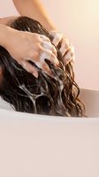 Woman washing long brown hair with shampoo foam in bathroom, hands massaging scalp during daily hygiene routine for healthy hair care and cleansing.