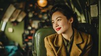 Young Asian woman pilot in vintage aircraft cockpit wearing brown leather jacket with confident expression looking away from camera.