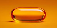 Transparent orange capsule pill on vibrant yellow background, pharmaceutical concept for health supplements and medication.