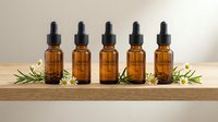 Five amber glass dropper bottles with essential oils arranged on wooden shelf with fresh green herbs and white flowers for aromatherapy wellness.