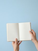 Open blank notebook held by two hands against light blue background, ready for writing, planning, journaling, or creative projects.