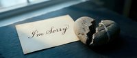Handwritten I'm Sorry note on aged paper beside a cracked stone heart on a dark surface, conveying regret, apology, and emotional healing.