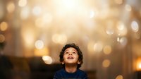 Young boy with curly dark hair and medium skin tone looking upward with wonder against warm golden bokeh lights, expressing hope and inspiration for motivational, educational, and aspirational content.
