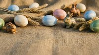 Colorful Easter eggs with wheat stalks and wooden bunny on rustic burlap background for spring holiday celebration and seasonal decoration projects.