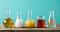 Laboratory glassware with colorful chemical solutions on wooden table against turquoise background for scientific research and education.