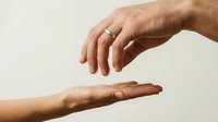 Two hands reaching toward each other in protective gesture against neutral background symbolizing care, support, trust and human connection.