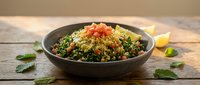 Fresh tabbouleh salad with parsley, tomatoes and bulgur wheat served in dark bowl on rustic wooden table with herbs and lemon wedges for healthy dining.