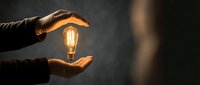 Close-up of hands holding glowing vintage filament lightbulb against dark background, symbolizing innovation, creativity, ideas, and sustainable energy solutions for business concepts.