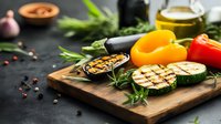 Grilled vegetables and spices on rustic wooden cutting board with fresh herbs, olive oil, and colorful bell peppers against dark background for food photography.