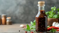 Homemade spicy sauce in glass bottle with fresh chili peppers, garlic and herbs on rustic wooden table against dark background. Food photography concept.