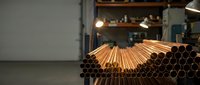 Stack of copper pipes in industrial warehouse with warm lighting creating manufacturing atmosphere for construction and plumbing projects.