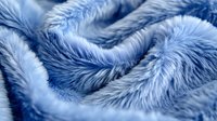 Soft plush blue faux fur fabric with waves and folds creating luxurious texture pattern, close up macro photography showing detailed fibers and pile.