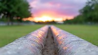 Dramatic sunset view along irrigation pipeline in rural farmland, with golden light reflecting off metal surface against pink and purple sky. Perfect for agriculture themes.