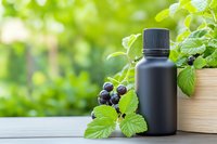 Black cosmetic bottle with blackcurrant berries and green leaves on wooden surface. Natural skincare product mockup for organic beauty treatments.