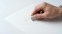 Hand using white eraser removing pencil marks from paper on clean desk surface for editing and correction work.